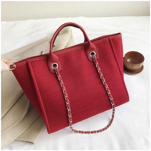 Close-up of red woven tote bag featuring silver chain decor and textured fabric detail