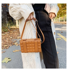 Detail of caramel brown box bag with plaid texture worn by a model in autumn street