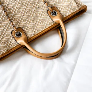 Detail of woven khaki bucket bag featuring leather handles and metal chain accents