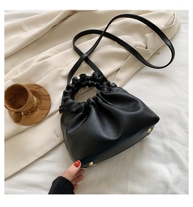 Detail of black cloud bucket bag showing gold metal base feet on beige suit fabric