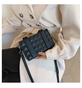 Detail of black quilted crossbody box bag with parallel straps on beige wool coat