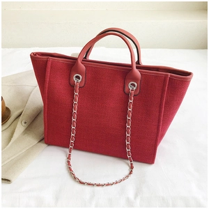 Close-up of red canvas tote bag with leather handles and silver metal chains