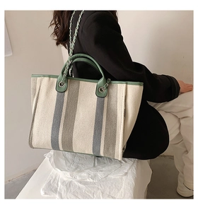 Detail of canvas tote bag with green stripes, leather trim and metal chain strap