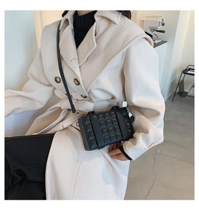 Detail of a black quilted box crossbody bag with parallel buckled straps on an overcoat