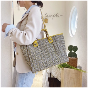 Close-up of woven tweed tote bag with yellow leather trim and metal chain strap detail