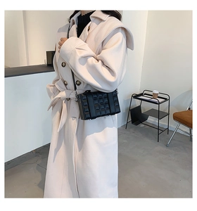 Detail of black box bag with textured checkered pattern on a beige wool coat