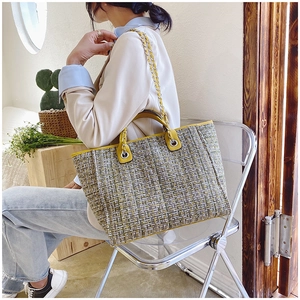 Detailed view of yellow and green tweed tote bag with metal chain strap on a model
