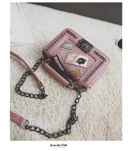 Detailed view of pink crossbody bag featuring metal rivets, chains and fashion patches