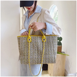 Detail of tweed tote bag featuring yellow leather trim and decorative silver chain strap