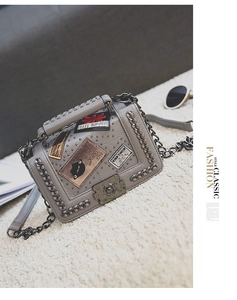 Close-up of grey square crossbody bag featuring metal badges and chain fringe details