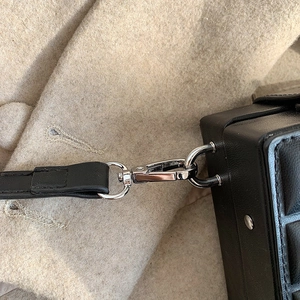 Close-up of silver metal clasp and leather texture on a black structured box bag