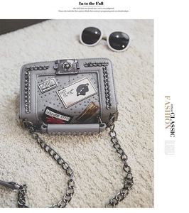 Close-up of grey square shoulder bag featuring retro patches, studs and metal chain detail