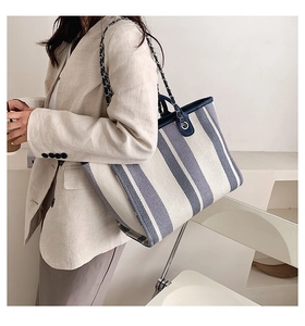 Détail du sac cabas en toile rayé bleu et blanc avec bandoulière chaîne sur une épaule