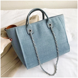 Detail of blue woven tote bag showing fine texture and silver chain strap with handle