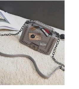 Close-up of a grey quilted small square bag with chain trim and decorative metal patches