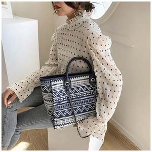 Detail of navy blue geometric woven tote bag with leather handles and chain strap