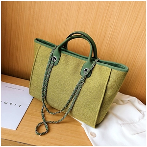 Close-up of green woven tote bag featuring silver chain strap and leather handle