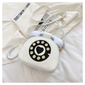 Close-up of a creative white vintage telephone-shaped crossbody bag with rotary dial detail