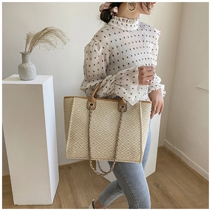 Detailed view of woven tote bag with beige diamond pattern and brown leather trim handles