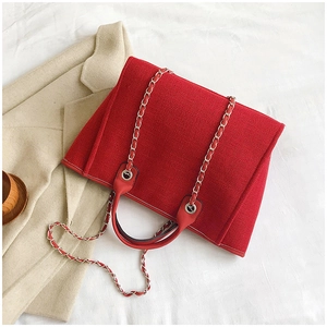 Detail of red canvas tote bag featuring premium leather handles and silver chain strap