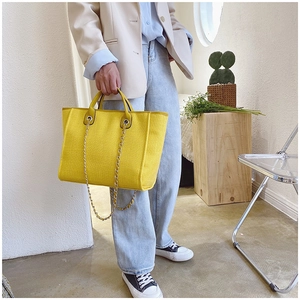 Detail of yellow woven tote bag with chain strap styled in a minimalist fashion setting