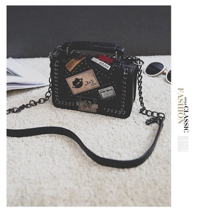Detail of black crossbody bag featuring punk graffiti patches and silver metal stud accents