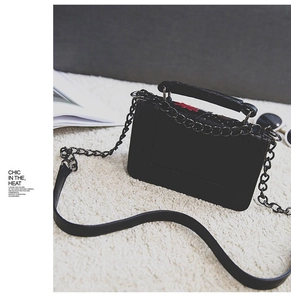 Fashionable black square handbag with colorful floral embroidery and metal chain on white rug