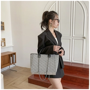 Detail of a large tote bag with black geometric patterns and a stylish metal chain strap
