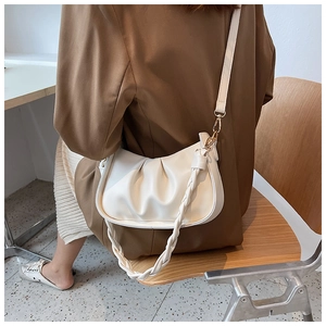 Détail d'un sac à bandoulière blanc cassé plissé avec poignée tressée porté par un modèle
