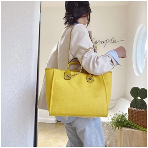 Detail of yellow large-capacity tote bag featuring gold chain strap and textured fabric