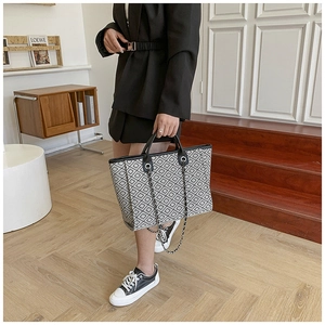 Chic monochrome tote bag featuring geometric patterns and a stylish chain strap on a model
