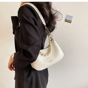 Détail du sac hobo crème avec chaîne en perles et bandoulière tressée sur un blazer noir