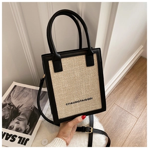Detail of beige woven mini tote bag with black PU leather trim and adjustable shoulder strap