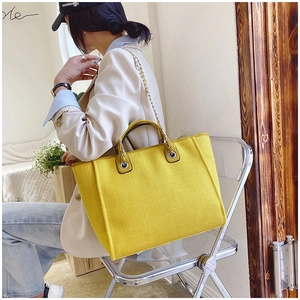 Detail of yellow woven tote bag with metal chain strap worn by a model in casual blazer