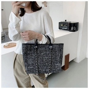 Close-up of black and white tweed tote bag with leather handle and metal chain detail