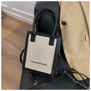 Detail of a two-tone beige woven tote bag with black leather trim and handles