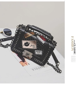 Detail of black crossbody bag with silver rivets, artistic patches and a metal lock