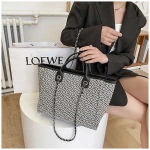 Detail of a geometric quilted tote bag with black leather handles and metal chain strap