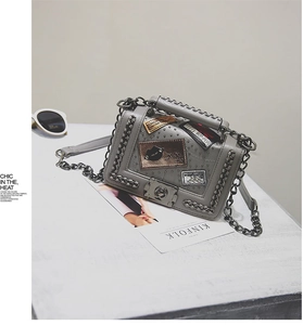 Close-up of gray PU leather square bag with metal chains, studs and trendy patches