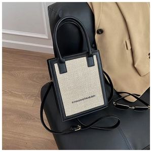 Detail of a chic tweed and black leather crossbody bag on a leather chair
