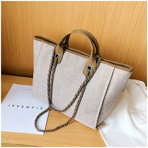 Detail of beige textured fabric tote bag with brown leather trim and chain strap