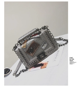 Detail view of grey crossbody bag featuring metallic chain and decorative patches
