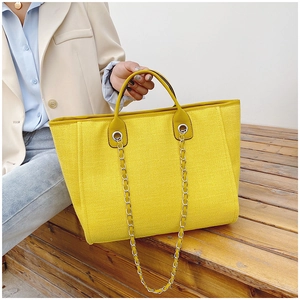 Close-up of yellow woven bucket bag with silver chain strap worn by a model