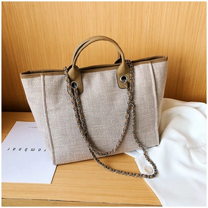 Detail of beige canvas tote bag with brown leather trim and metal chain strap