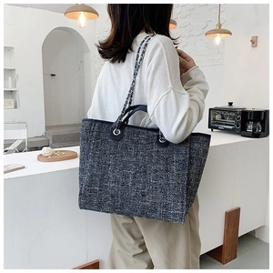 Detail view of a large tweed tote bag with leather handles and woven chain shoulder strap