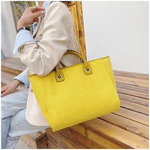 Detail of yellow woven bucket bag with silver chain strap shown on model's shoulder