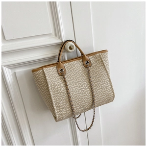 Detail of woven tote bag with geometric texture, leather handles and chain strap