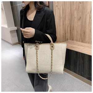 Detail of beige woven tote bag featuring brown handles and classic metal chain strap