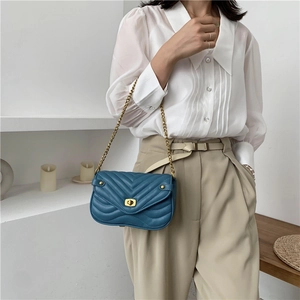 Sac bandoulière bleu marine à surpiqûres en V et fermoir doré porté par un mannequin