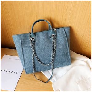 Detail of light blue woven tote bag with metal chain strap on a rustic wooden desk